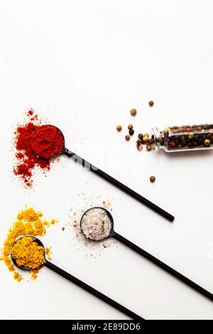 Various spices in black spoons. Salt, curry, turmeric, ground paprika, bay leaf, garlic, peppercorns flat lay on a white background Stock Photo
