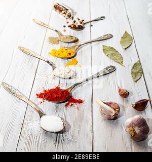 Various spices in vintage spoons, selective focus, close-up. Salt, curry, turmeric, ground pepper, ground paprika, bay leaf, garlic, peppercorns flat Stock Photo