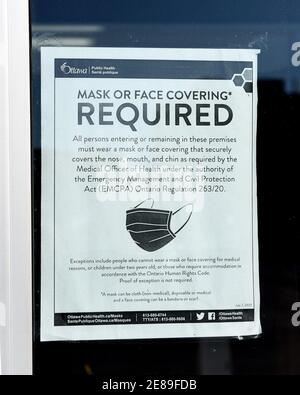 Ottawa, Canada - January 30, 2021: Sign on the door on store window stating the details of the mask bylaw created by Ottawa Public Health. Stock Photo