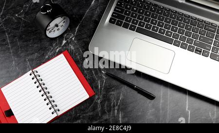 A laptop, clock and notebook on the black rough marble surface. Time management concept. Selective focus Stock Photo