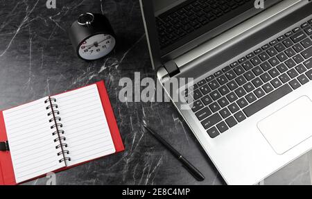 A laptop, clock and notebook on the black rough marble surface. Time management concept. Selective focus Stock Photo