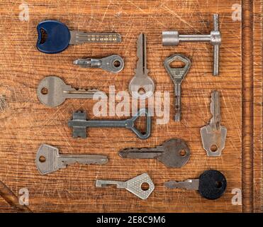 Many assorted old multi-colored metal antique vintage keys of different shapes on wooden scratched table background. Home security concept. Stock Photo