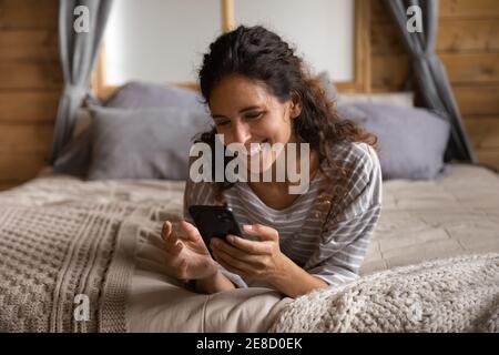 Close up smiling attractive woman using phone, lying on bed Stock Photo