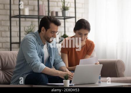 Serious young couple using laptop, checking financial documents together Stock Photo