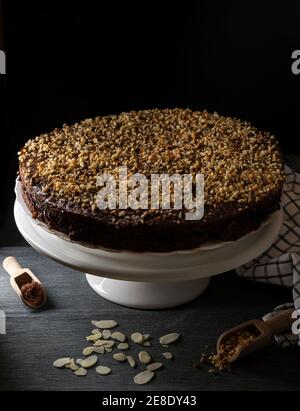 A cocoa cake filled with fruit jam and covered with chopped hazelnuts on a white stand and black background Stock Photo