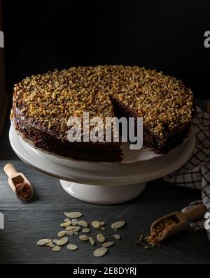 A cocoa cake filled with fruit jam and covered with chopped hazelnuts on a white stand and black background Stock Photo