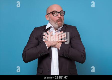 Mature amazed man keeps hands on chest pleased to recieve good news. Studio shot Stock Photo
