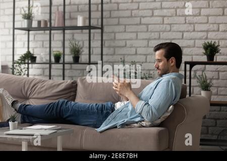Side view man wearing glasses using phone, lying on couch Stock Photo
