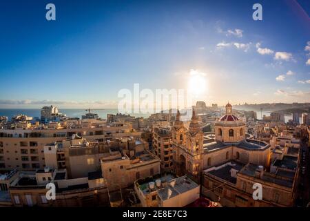 Sunrise in malta. rooftop view from sliema with a church in the foreground and blue sky and sun rising in the background Stock Photo