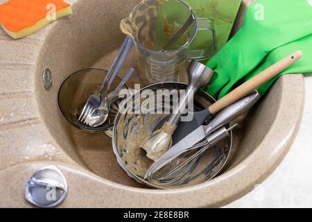 Unwashed dishes and utensils in kitchen sink, latex gloves and washing sponge Stock Photo