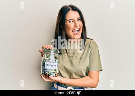 Middle age brunette woman holding charity jar with money smiling and laughing hard out loud because funny crazy joke. Stock Photo