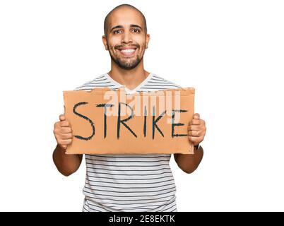 Hispanic adult man holding strike banner cardboard looking positive and happy standing and smiling with a confident smile showing teeth Stock Photo