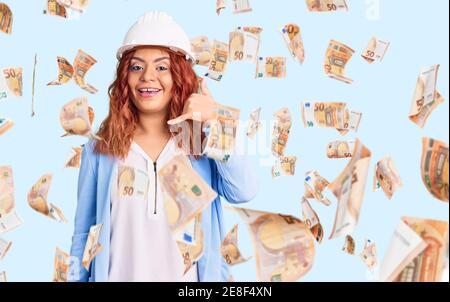 Young latin woman wearing architect hardhat smiling doing phone gesture with hand and fingers like talking on the telephone. communicating concepts. Stock Photo