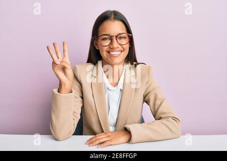 Beautiful hispanic woman working at the office showing and pointing up with fingers number three while smiling confident and happy. Stock Photo