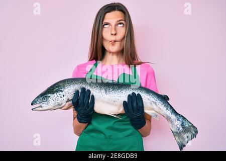 Beautiful brunettte woman professional chef holding fresh salmon fish  making fish face with mouth and squinting eyes, crazy and comical Stock  Photo - Alamy