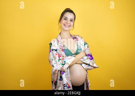 Young beautiful woman pregnant expecting baby wearing pajama over isolated yellow background with a happy face standing and smiling with a confident s Stock Photo