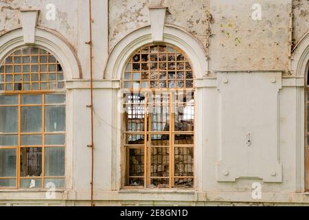 Broken and covered with metal bars windows of an old crumbling house Stock Photo