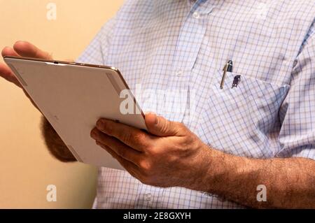 An unrecognizable man wearing a shirt, holding a tablet and working Stock Photo