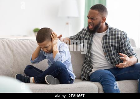 Angry African Father Shouting At Scared Son Sitting At Home Stock Photo