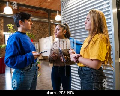 Young female classmates in casual wear standing close while talking about studying in corridor of university Stock Photo