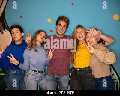 Happy young women and man smiling brightly while standing together against colorful painted wall and looking at camera Stock Photo