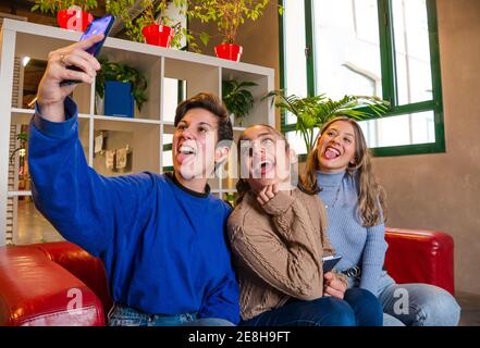 Smiling female students sitting on sofa with notebook and taking self portrait on mobile phone during break Stock Photo