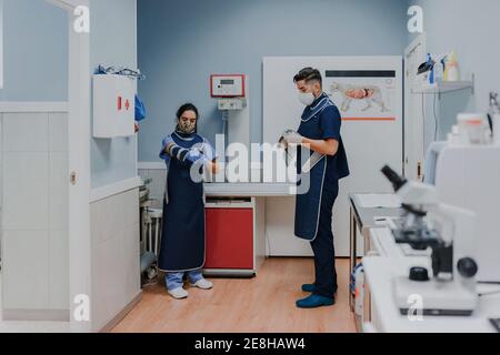 Unrecognizable young male vet in sterile mask and gloves standing near female colleague while preparing for work in lab Stock Photo