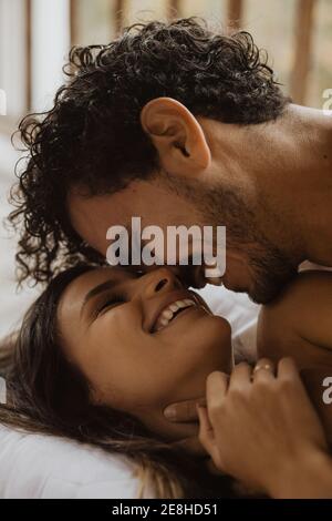 Cheerful young couple bonding and smiling happily while lying on soft cozy bed Stock Photo