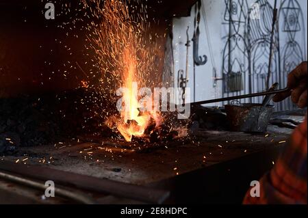 Crop unrecognizable male blacksmith heating metal rod on burning flame during forging process in workshop Stock Photo