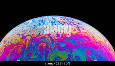 Panoramic view of closeup bubble textured backdrop representing colorful planet with wavy lines on round shaped surface on black background Stock Photo