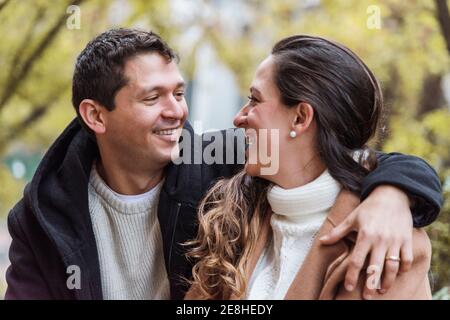 Cheerful young couple in warm clothes hugging tenderly and looking at each other with affection while standing together on street Stock Photo