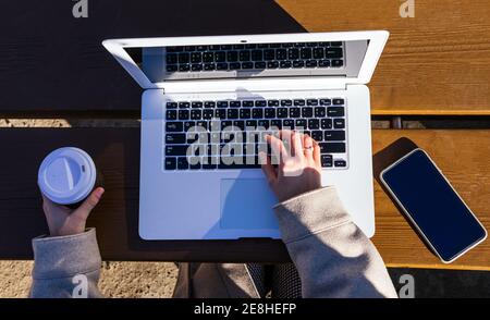Top view of unrecognizable young Woman using her laptop on the street at a table while having coffee Stock Photo