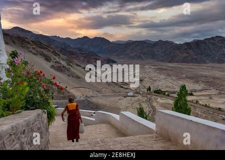 Thikse, India - August 24, 2015: An elder monk at goes down the stairs of Thikse Monastery at sunrise. Thikse Monastery is located on top of a hill Stock Photo