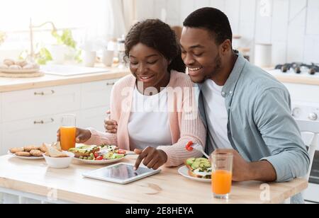 Happy Black Couple Using Digital Tablet While Having Breakfast In Kitchen Stock Photo