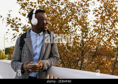 Side view of content African American male manager in headset text messaging on cellphone near fence in town Stock Photo