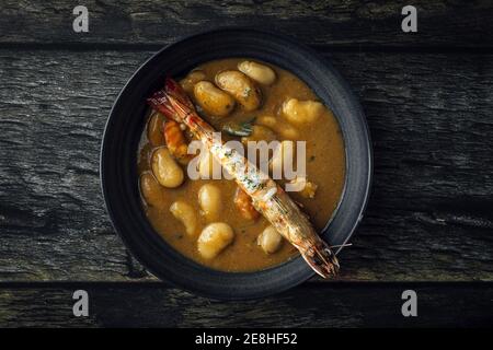From above of appetizing cream soup with white beans and langoustines served in bowl and placed on wooden tabletop in kitchen Stock Photo