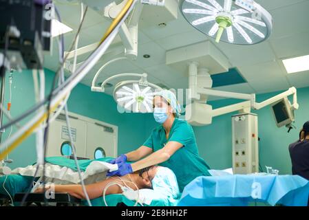 Low angle of anonymous concentrated female nurse in uniform and mask covering unrecognizable patient with sterile blanket before surgery in modern hos Stock Photo