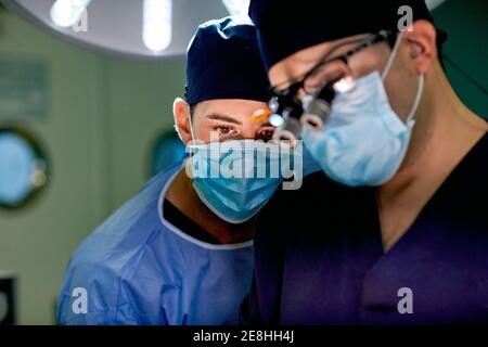 Unrecognizable young attentive male practitioner in sterile gown and mask following operation process performing by professional doctor in modern clin Stock Photo