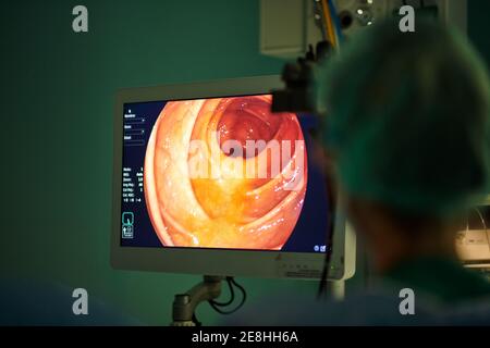 Back view of unrecognizable female doctor in uniform looking at monitor while performing endoscopic surgery in modern operating room Stock Photo
