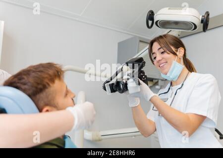 Smiling competent female dentist taking photos of male patient teeth while working in contemporary equipped dental clinic Stock Photo
