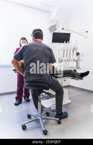 Unrecognizable dentist in uniform examining patients teeth near nurse in modern equipped dental clinic Stock Photo