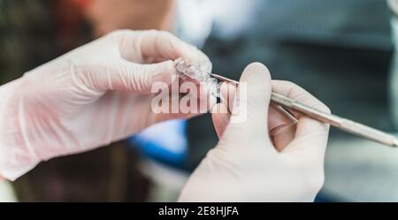 Crop unrecognizable dentist in latex gloves holding ultra thin veneers and scaler while working in dental clinic Stock Photo