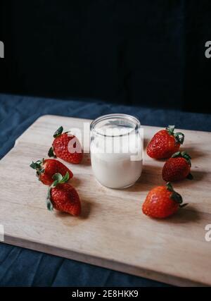 From above of transparent glass jar of milk near fresh sweet strawberries for smoothie on black background Stock Photo