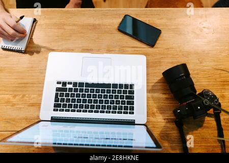 From above of crop male baristas sitting at wooden counter in coffee shop and working together while using laptop and taking notes in notebook Stock Photo