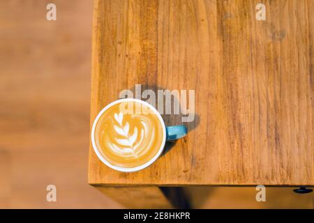 Top view of mug of cappuccino with coffee art on foam placed on wooden table in cafe Stock Photo