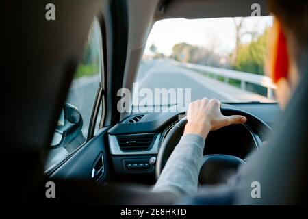Back view of crop unrecognizable male driving a modern car on sunny day on motorway Stock Photo