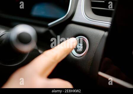 Closeup of crop anonymous male pressing Start Engine Stop button while sitting in modern car before driving Stock Photo