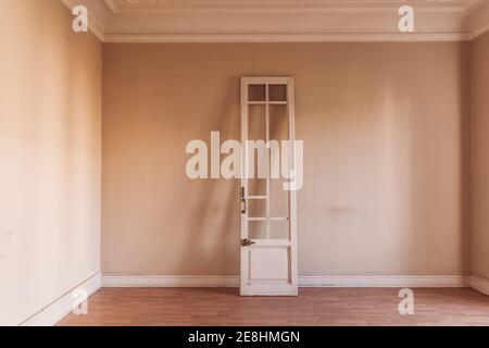 White wooden door with shabby surface placed in old empty room at daytime Stock Photo