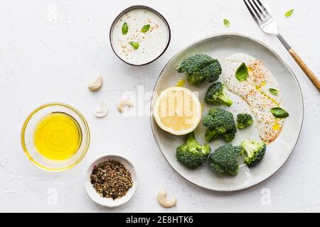 Top view of tasty broccoli with fresh lemon and sauce near bowls with olive oil and spice mix on table Stock Photo