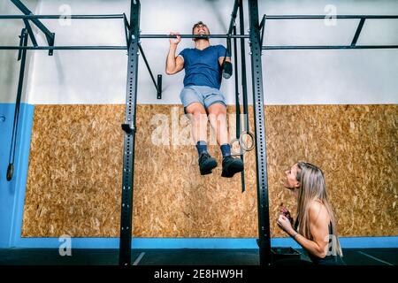 Young female athlete training and helping handicapped sportsman on horizontal bar during training in gym Stock Photo
